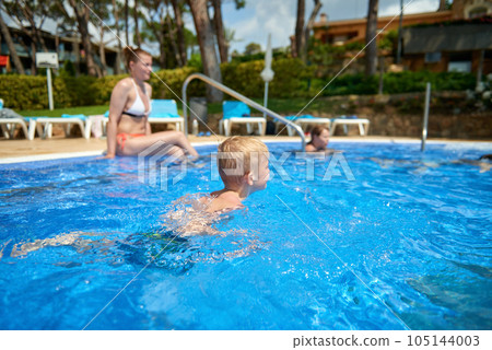 Young boy kid child eight years old splashing in swimming pool having fun leisure activity. Boy happy swimming in a pool. Activities on the pool, children swimming and playing in water, happiness and Young boy kid child eight years old splashing in swimming pool having fun leisure activity. Boy happy swimming in a pool. Activities on the pool, children swimming and playing in water, happiness and 105144003
