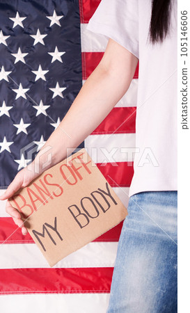 Woman holding a sign Bans Off My Body American flag on background. Protest against anti abortion law. Women's strike. Womens rights freedom. Woman holding a sign Bans Off My Body American flag on background. Protest against anti abortion law. Women's strike. Womens rights freedom. 105146606