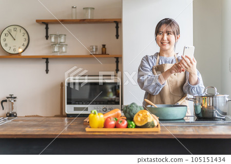 一位亞洲家庭主婦使用智能手機搜索食譜並在廚房使用烹飪應用程序 一位亞洲家庭主婦使用智能手機搜索食譜並在廚房使用烹飪應用程序 105151434