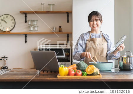 A woman cooking while watching a recipe video on her computer A woman cooking while watching a recipe video on her computer 105152016