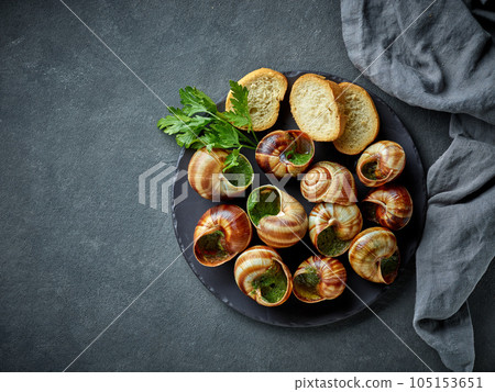 plate of baked escargot snails filled with parsley and garlic butter 105153651