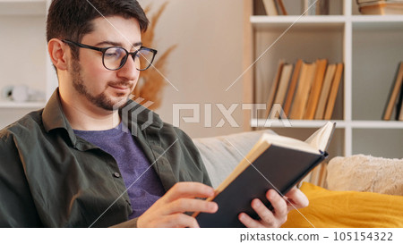 Reading hobby. Interesting book. Literature intelligence. Smart relaxed man enjoying paper bestseller story on couch in light interior at home. Reading hobby. Interesting book. Literature intelligence. Smart relaxed man enjoying paper bestseller story on couch in light interior at home. 105154322