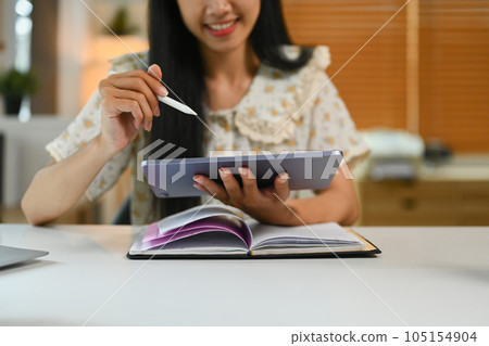 Cropped shot of young woman sitting in home office and using digital tablet. Technology, freelance work and lifestyle concept 105154904