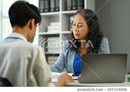 Mature businesswoman wearing elegant suit analyze the results and discussing them on financial operations with young employee 105154906