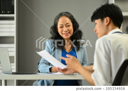 Positive mature businesswoman listening attentively, discussing financial reports with young male employee at office Positive mature businesswoman listening attentively, discussing financial reports with young male employee at office 105154916