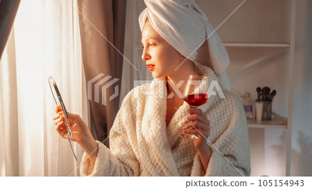 Morning spa. Beauty routine. Luxury weekend. Confident woman in bathrobe towel with red wine alcohol drink glass mirror in light home interior with free space. Morning spa. Beauty routine. Luxury weekend. Confident woman in bathrobe towel with red wine alcohol drink glass mirror in light home interior with free space. 105154943