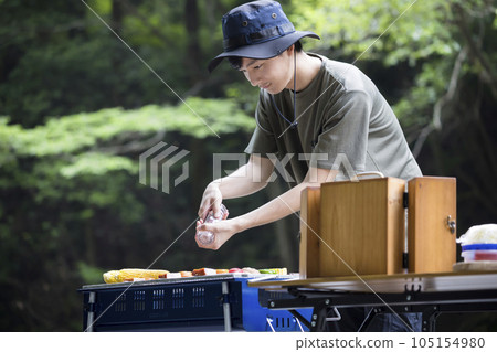 Barbecue image A young man sprinkling salt on skewers Barbecue image A young man sprinkling salt on skewers 105154980