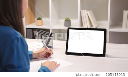 Video chat. Online education. Home study. Distance learning. Woman student at digital class lecture at tablet with empty space white mockup screen writing notes in modern interior. 105155013