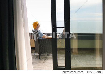 Young man in gray casual clothes and yellow hat sits on wicker chair and holds glass of champagne. 105155980