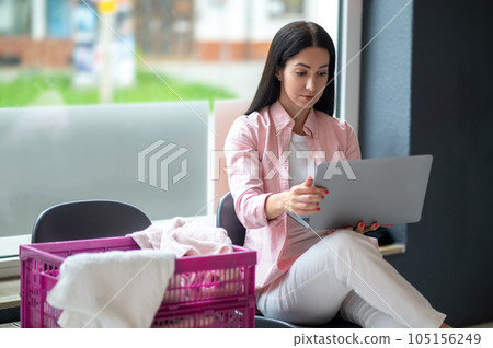 Woman with laptop at laundromat doing job project, connection and multitask, working on computer while washing clothes. 105156249