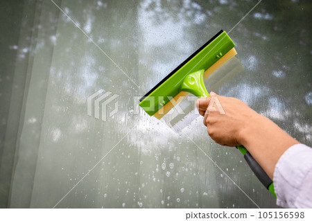 A woman cleans windows with a squeegee A woman cleans windows with a squeegee 105156598