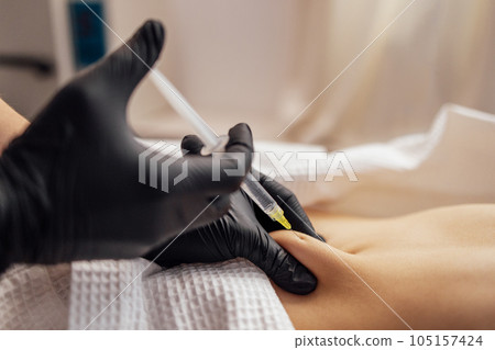 Close up of hands in black gloves of cosmetologist giving injection into stomach of client. Close up of hands in black gloves of cosmetologist giving injection into stomach of client. 105157424