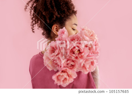 Beautiful african girl holds a bouquet of pink flowers near her face 105157685