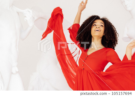 Attractive black girl in red flying dress among antique white statue Attractive black girl in red flying dress among antique white statue 105157694
