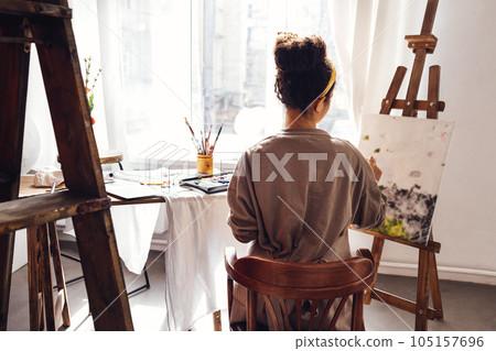 Young female creative pretty african american artist paints picture with oil paints in art studio 105157696