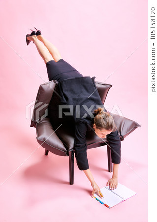 Woman weirdly lying on armchair, looking through working plan and notes, working on floor against pink studio background Woman weirdly lying on armchair, looking through working plan and notes, working on floor against pink studio background 105158120