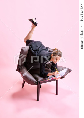 Anger and irritation. Business Woman lying on armchair in weird pose and putting notes on against pink studio background 105158127