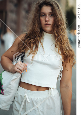 A chic girl wearing white clothes and sporting curly hair on the city streets. 105158190