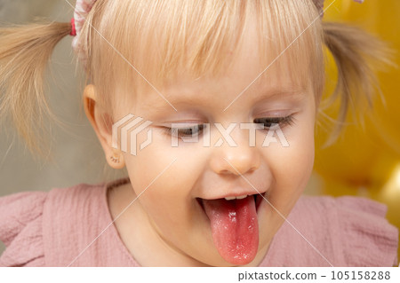 Little girl with red tongue from dye after eating cake. Little girl with red tongue from dye after eating cake. 105158288