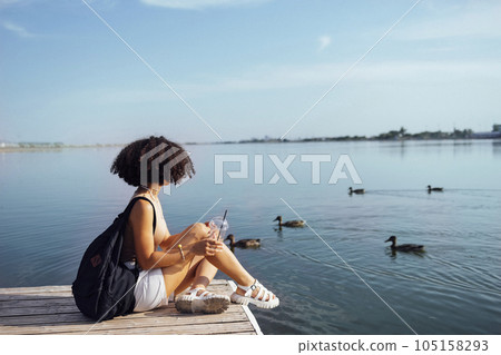 Beautiful mixed race female teenager sits on wooden pier Beautiful mixed race female teenager sits on wooden pier 105158293