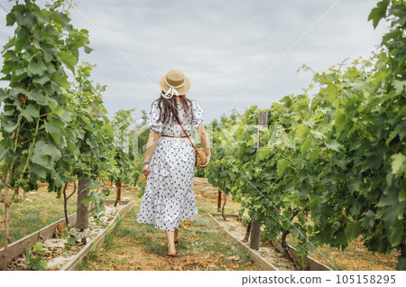 Woman, wearing a hat, in a vineyard in the sun Woman, wearing a hat, in a vineyard in the sun 105158295