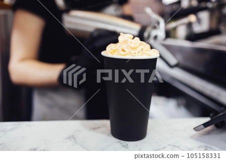 Brunette female barista decorates milk cocktail with cream using pastry nozzle. Brunette female barista decorates milk cocktail with cream using pastry nozzle. 105158331