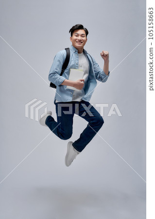 Full length of a smiling young asian man carrying backpack isolated, holding books, jumping Full length of a smiling young asian man carrying backpack isolated, holding books, jumping 105158663