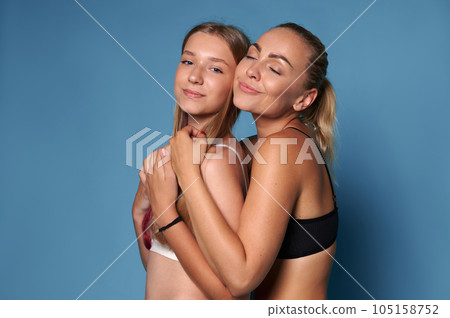 Happy young pretty woman mother in underwear, with perfect clean flawless glowing skin, hugging her adolescent daughter 105158752