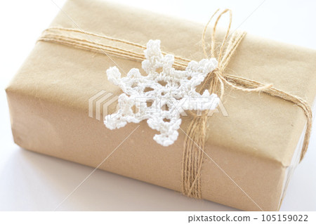 Christmas and New Year background. Gift box wrapped in kraft paper with jute cord. Decorated with a crocheted snowflake 105159022
