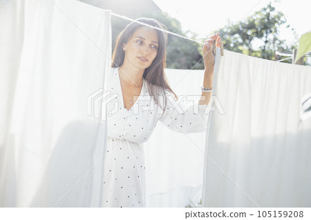 A charming young woman in a white dress is hanging up the washing. 105159208