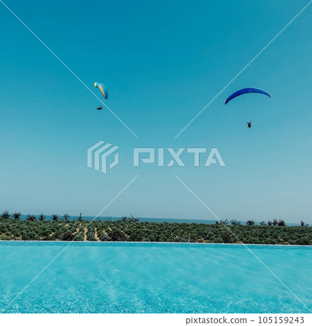 Two paragliders fly against the blue sky and azure water in the pool. 105159243
