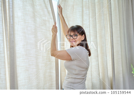 Back view, woman closes light curtains in the living room Back view, woman closes light curtains in the living room 105159544