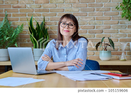 Middle-aged business woman office worker, manager looking at camera sitting at a desk 105159606