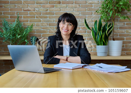 Mature business woman sitting at work desk with computer papers 105159607