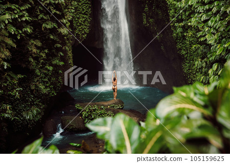 Scenic waterfall and woman in bikini. Traveler girl posing on waterfall Scenic waterfall and woman in bikini. Traveler girl posing on waterfall 105159625
