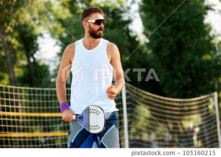 Bearded man in sunglasses going on beach to play paddle tennis on warm summer day. Outdoor activity 105160215