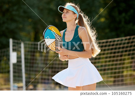 Concentrated beautiful woman standing near net, platong paddle tennis on beach on warm summer day. Outdoor game Concentrated beautiful woman standing near net, platong paddle tennis on beach on warm summer day. Outdoor game 105160275