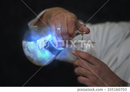 Chemical flask with a blue solution and a mystical glow in the hands of a laboratory assistant. Experiences and experiments. Chemical flask with a blue solution and a mystical glow in the hands of a laboratory assistant. Experiences and experiments. 105160703