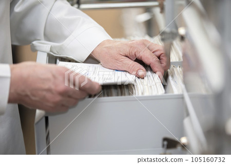 The nurse's hands are looking in the archive for a patient's card. The file is in a cell in the clinic. 105160732