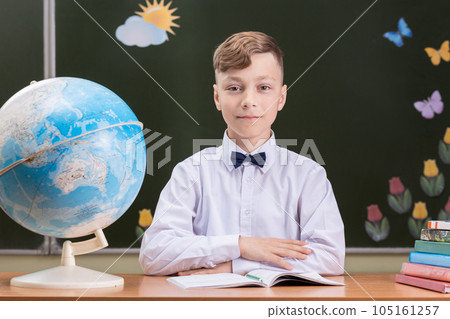 A beautiful happy schoolboy is sitting at a desk 105161257