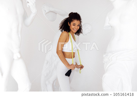 Slim young afro woman in white top and leggings with jump rope on her neck Slim young afro woman in white top and leggings with jump rope on her neck 105161418