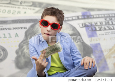 A cute, rich boy in glasses holds dollars and knows how to make money against the background of falling banknotes. Money rain, Financial education, young millionaire, investments, loans, winnings A cute, rich boy in glasses holds dollars and knows how to make money against the background of falling banknotes. Money rain, Financial education, young millionaire, investments, loans, winnings 105161925