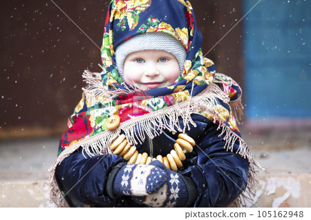 A little girl in a Russian headscarf with bagels at the Maslenitsa holiday. 105162948