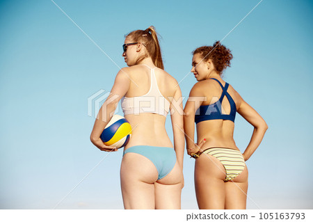 Back view image of sportive young women, with fit, slim body in swimsuit standing with volleyball ball over blue sky background Back view image of sportive young women, with fit, slim body in swimsuit standing with volleyball ball over blue sky background 105163793