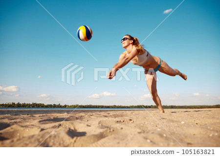 Dynamic image of young woman in motion, playing beach volleyball, hitting ball and falling down on sand 105163821