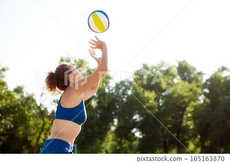 Young woman playing beach volleyball on sunny day, serving ball with hands. Outdoors training on fresh air Young woman playing beach volleyball on sunny day, serving ball with hands. Outdoors training on fresh air 105163870