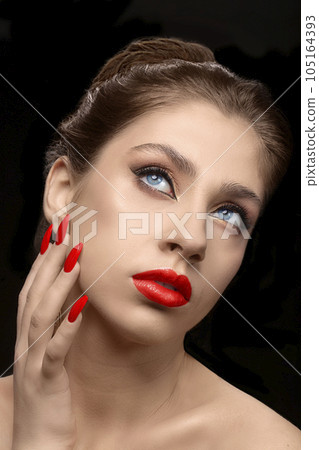 Model with red lipstick and beautiful manicure on a dark background. The face of a beautiful well-groomed brunette girl with clean skin. 105164393