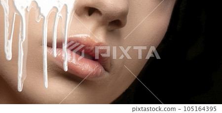 White paint or face cream dripping from the lips. White liquid smudges on the mouth of a beautiful model girl. Skin care. 105164395