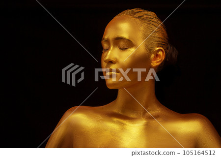Model girl with golden professional art make-up on a black background. Beautiful golden metallic body, lips and skin 105164512