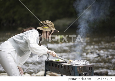 A young woman seriously having a barbecue on the riverbed A young woman seriously having a barbecue on the riverbed 105165796
